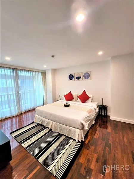 Condominium for rent in Bang Rak, Bangkok - Bedroom with king bed, striped rug, and balcony-height windows.