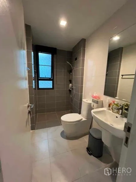 Detached House for sale in Khan Na Yao, Bangkok - Contemporary bathroom with gray tiled shower area, toilet and wall-mounted sink with mirror.