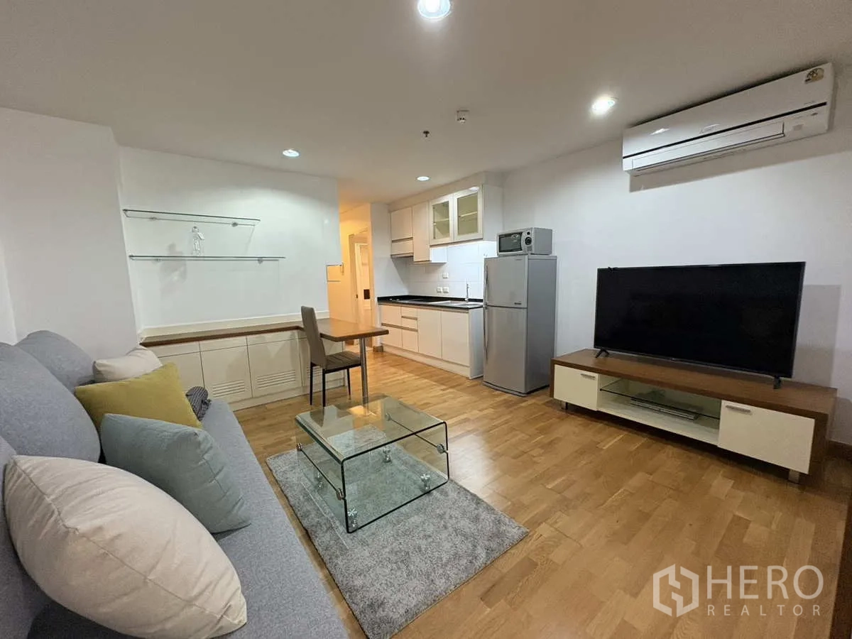 Condominium for rent in Khlong Toei, Bangkok - Open‑plan lounge with TV, air‑conditioning, compact kitchen and glass coffee table.