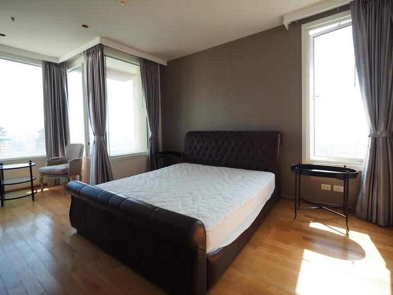 Condominium for rent in Sathon, Bangkok - Corner master bedroom with tall windows, tufted leather bed, side tables and city views.