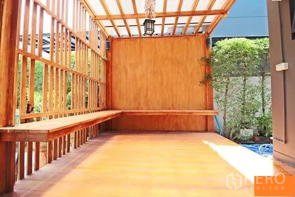Detached House for rent in Bang Khae, Bangkok - Covered wooden terrace with slatted walls and built‑in bench beside a small garden.