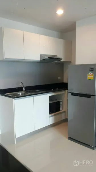 Condominium for rent in Phaya Thai, Bangkok - Modern kitchen featuring white cabinetry, sink, cooktop with hood, microwave niche and a large fridge.