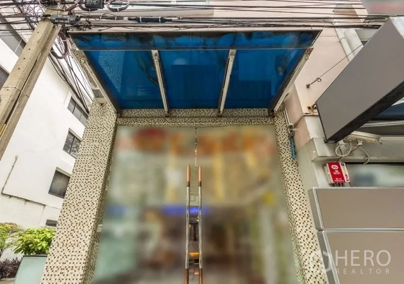 Retail Space for rent - Glass-front retail entrance with a blue canopy and double doors on a lively Bangkok lane.