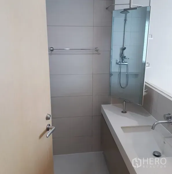 Condominium for rent in Khlong Toei, Bangkok - Contemporary bathroom with long vanity, wall mirror, towel rail, and a glass shower with rainfall head.