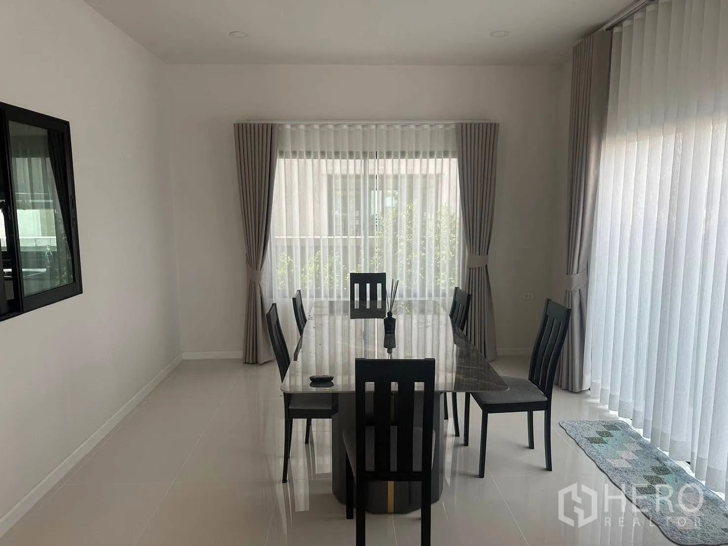 Detached House for rent in Bang Phli, Samut Prakan - Light‑filled dining area with a long table and six chairs surrounded by large curtained windows.