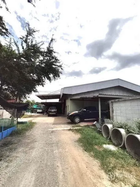 Factory for sale in Lat Lum Kaeo, Pathum Thani - Lat Lum Kaeo factory exterior with metal roof, gravel driveway, boundary wall and parking under cloudy sky.