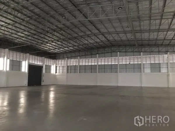 Factory for rent in Samut Prakan - Spacious warehouse interior with high clear-span steel truss roof, smooth concrete floor and vented walls.