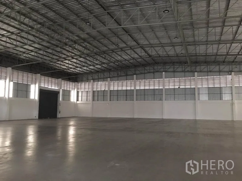 Factory for rent in Samut Prakan - Spacious warehouse interior with high clear-span steel truss roof, smooth concrete floor and vented walls.
