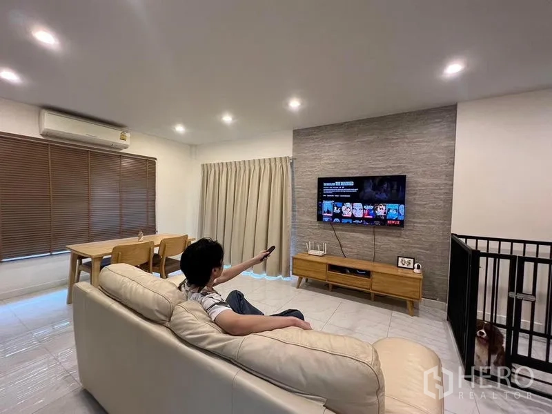 Detached House for sale in Bang Kruai, Nonthaburi - Living area with TV feature wall, sofa and dining set under recessed lighting.