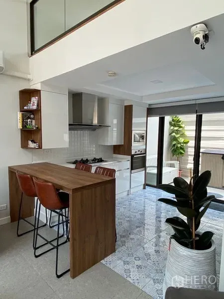 Townhouse for rent in Suan Luang, Bangkok - Modern kitchen with breakfast bar, white cabinetry, gas hob and sliding glass doors to the patio.