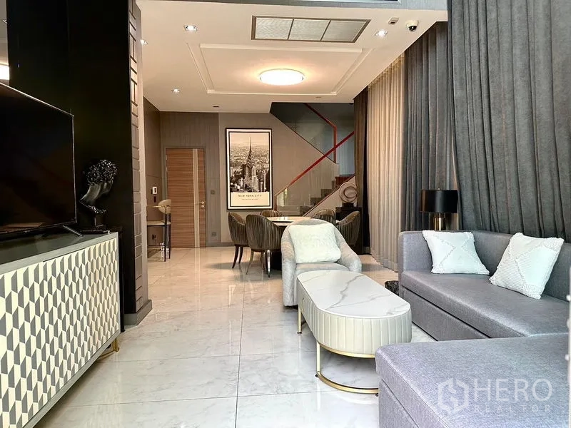 Detached House for rent in Phra Khanong, Bangkok - Open-plan living and dining area with high ceilings and gray sectional sofa.