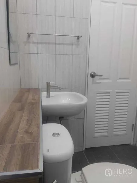 Detached House for sale in Phra Khanong, Bangkok - Compact bathroom with light wall tiles, basin, toilet and wooden countertop.