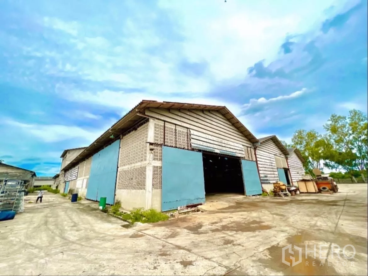 Factory for rent in Sai Noi, Nonthaburi - Gable-end warehouse blocks with blue sliding doors and a truck-access driveway.