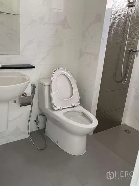 Home Office for rent or sale in Suan Luang, Bangkok - Modern restroom with sink, toilet, handheld bidet and walk-in shower with wall-mounted showerhead.