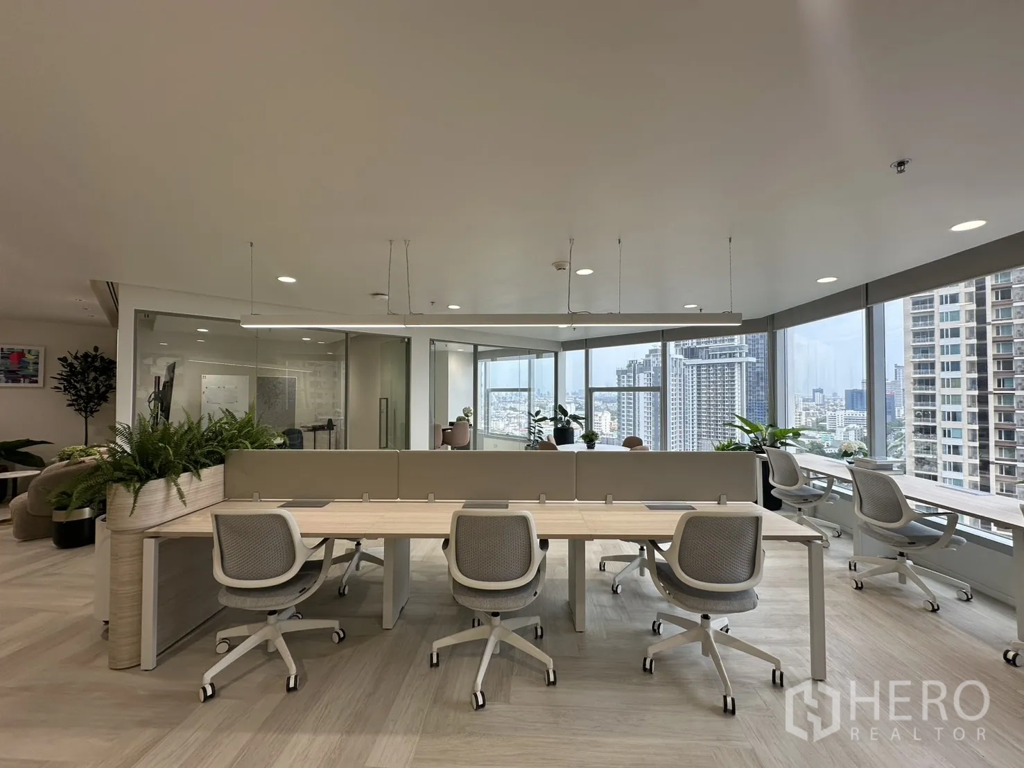 办公室 for rent in Sathon, Bangkok - 开放式办公室，长排工位与人体工学椅，玻璃房间、绿植与落地窗外城市景观。