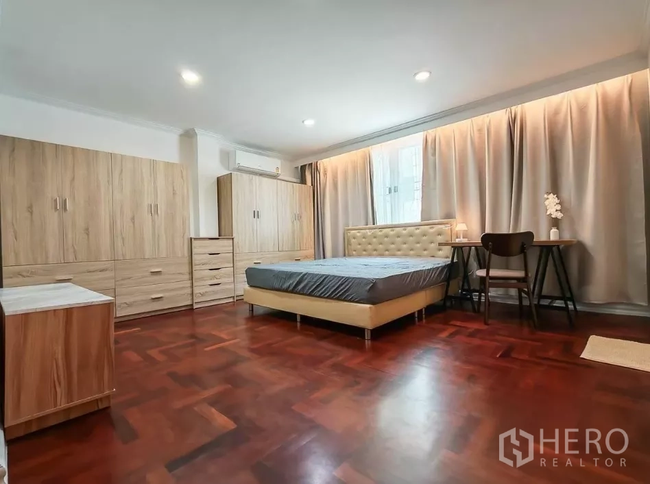 Detached House for rent in Yan Nawa, Bangkok - Spacious bedroom with parquet floors, multiple wardrobes, and a tufted bed beside a desk.