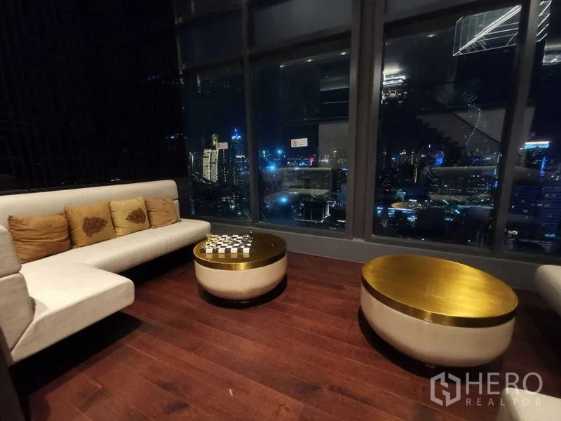 Condominium for rent in Ratchathewi, Bangkok - Night lounge with sofa and gold coffee tables facing floor-to-ceiling city views.