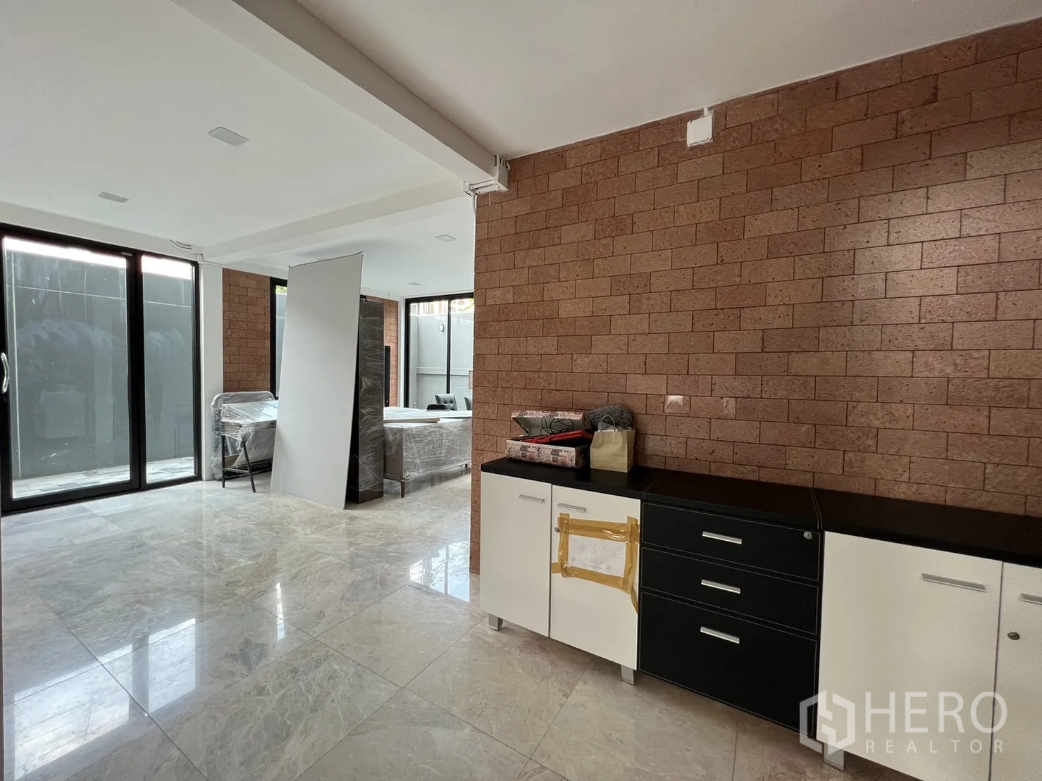 Detached House for rent or sale in Phra Khanong, Bangkok - Open-plan area with built-in cabinets and exposed brick wall.