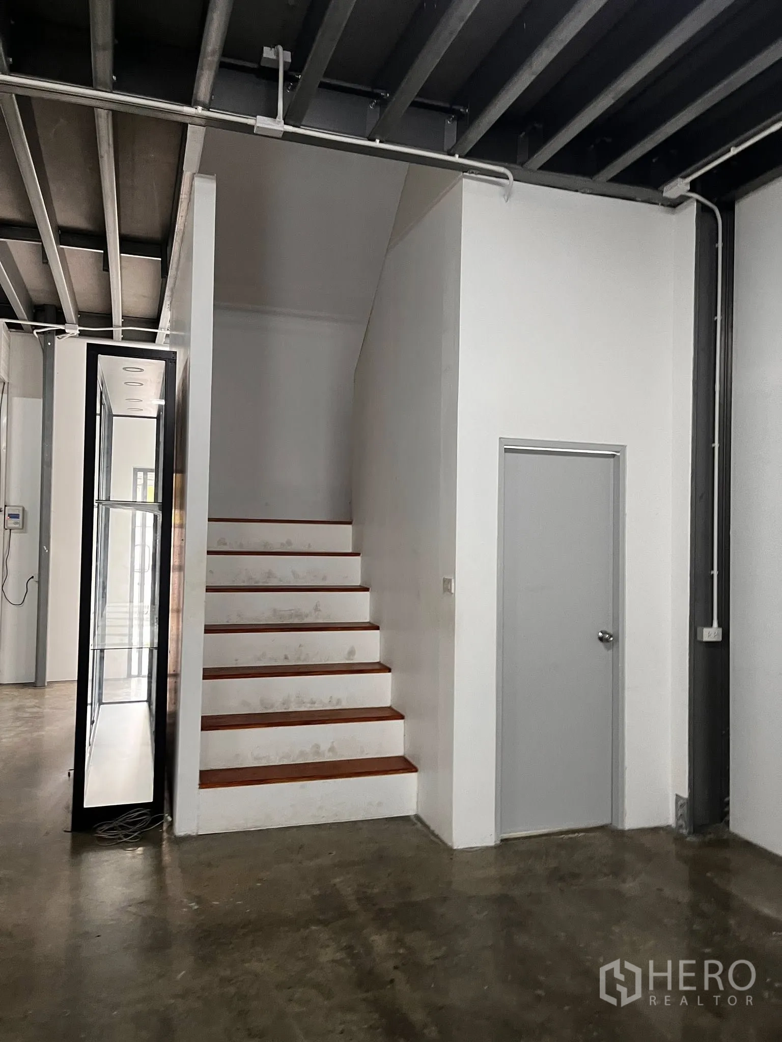 Warehouse for rent in Lat Phrao, Bangkok - Interior view showing a staircase to the upper level and a side door near the glass entry.