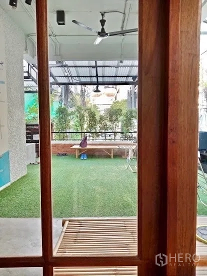 店屋 出租在Pathum Wan, Bangkok - 透过木框望向半室外草坪区，顶部风扇与绿植围栏。