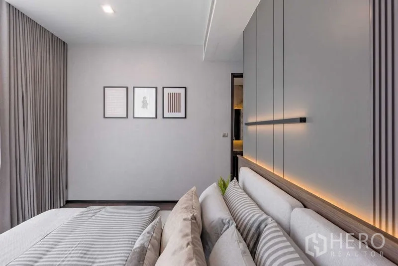 Condominium for rent in Watthana, Bangkok - Bedroom detail showing wall panels, framed art and layered pillows on the bed.