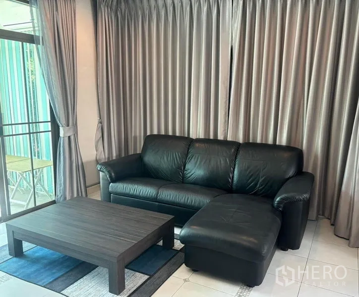 独立式住宅 出租在Bang Phli, Samut Prakan - L型黑色皮沙发与茶几，前方为整面窗帘