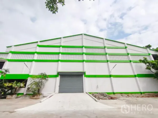 Factory for sale in Samut Prakan - Green-and-white factory facade with roller shutter door and loading ramp in Bang Sao Thong, Samut Prakan.