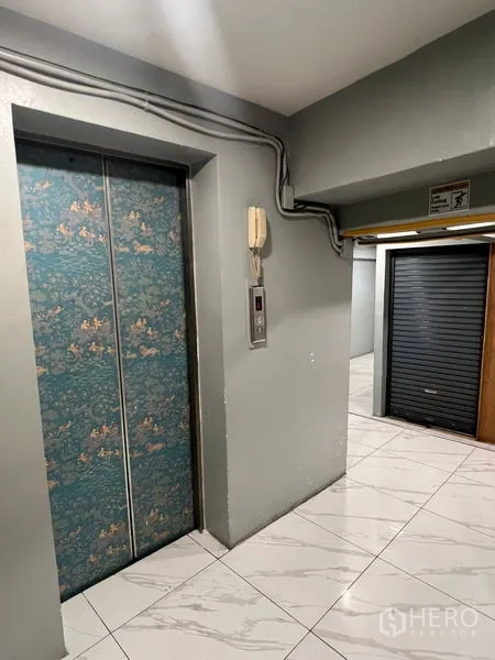 零售空间 出租在Khlong Toei, Bangkok - 电梯前厅，花纹电梯门与瓷砖地面，旁有卷闸门。