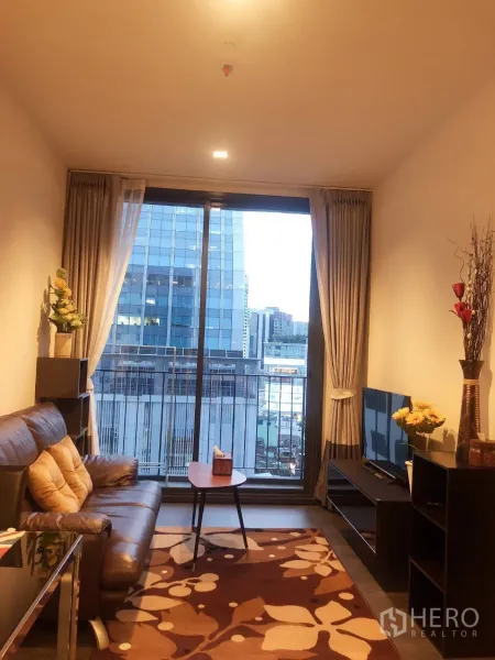 Condominium for rent in Watthana, Bangkok - Living room with leather sofa, TV console, rug and floor-to-ceiling sliding door to a balcony with city view.