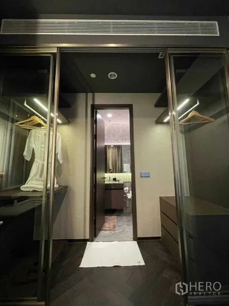 Condominium for rent in Khlong Toei, Bangkok - Walk‑in closet with glass wardrobes and hanging rails leading through to the bathroom.
