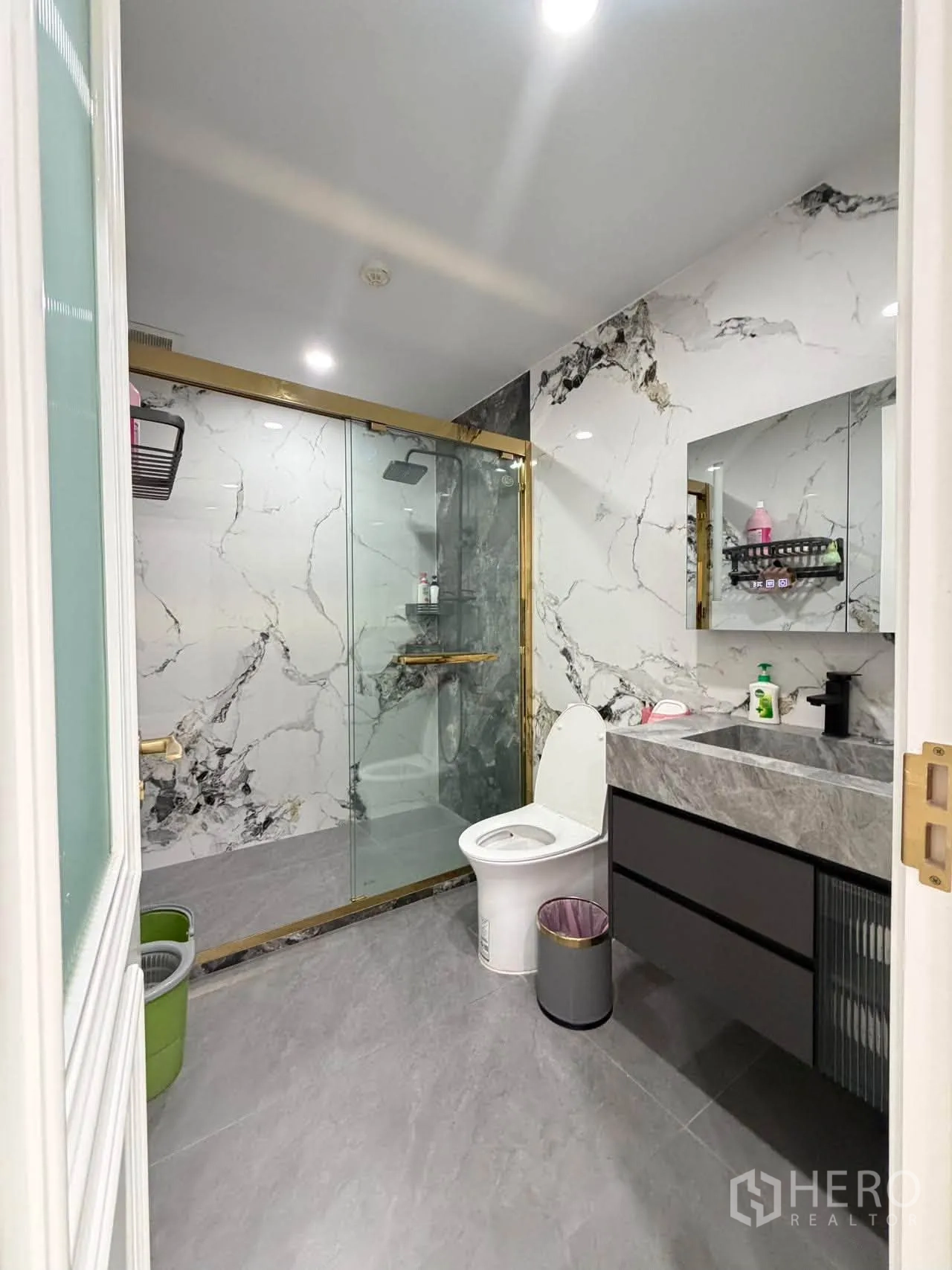 Condominium for sale in Watthana, Bangkok - Bathroom with marble-pattern walls, gold-trim shower, and modern vanity.