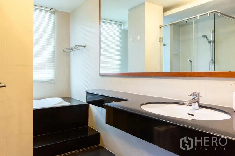 Condominium for rent in Bang Rak, Bangkok - Modern bathroom featuring a long vanity, soaking tub by the window and a glass-enclosed shower.
