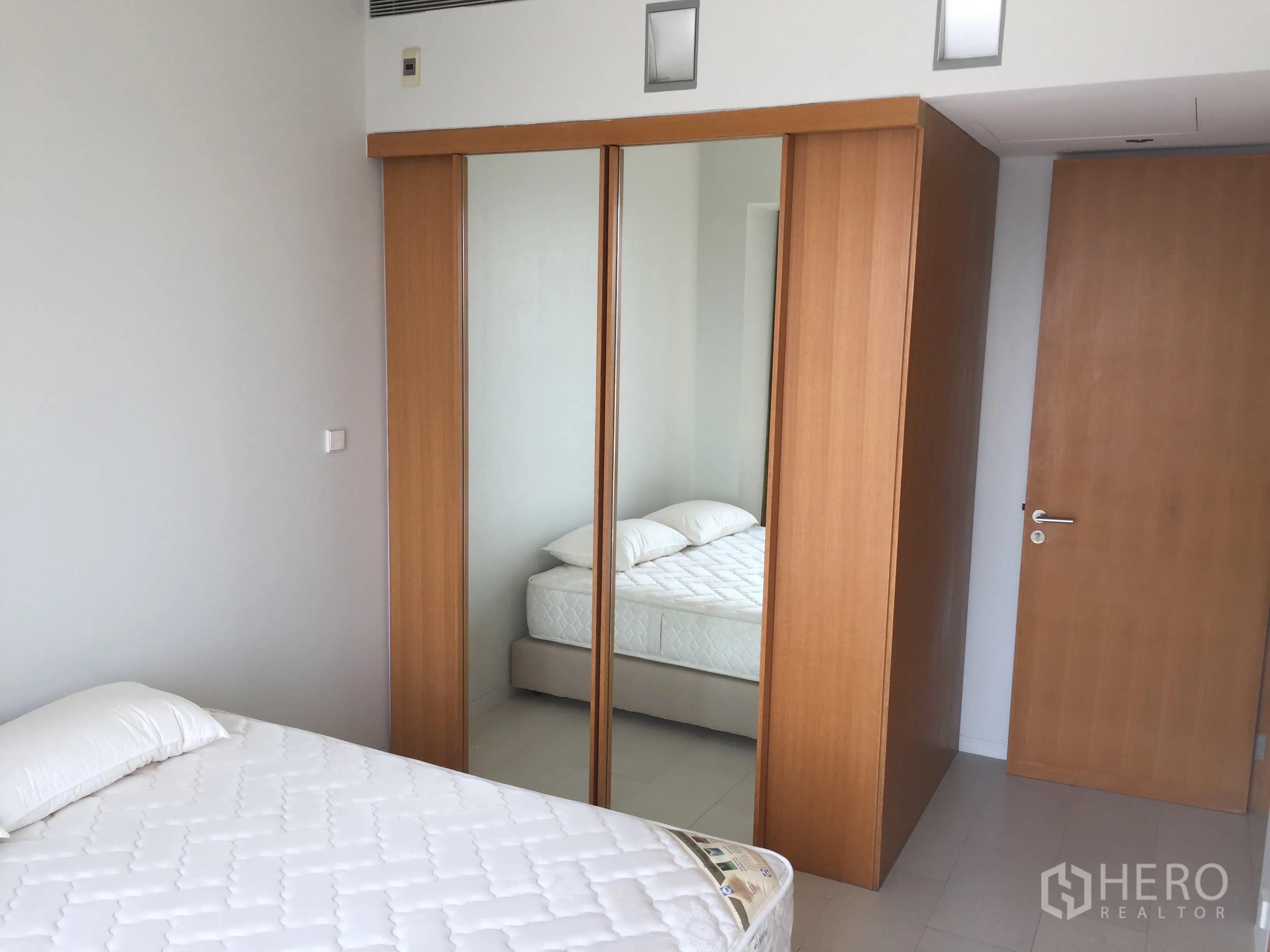 Condominium for rent in Sathon, Bangkok - Bright bedroom in a Sathon condo with mirrored wooden wardrobe and minimalist decor.