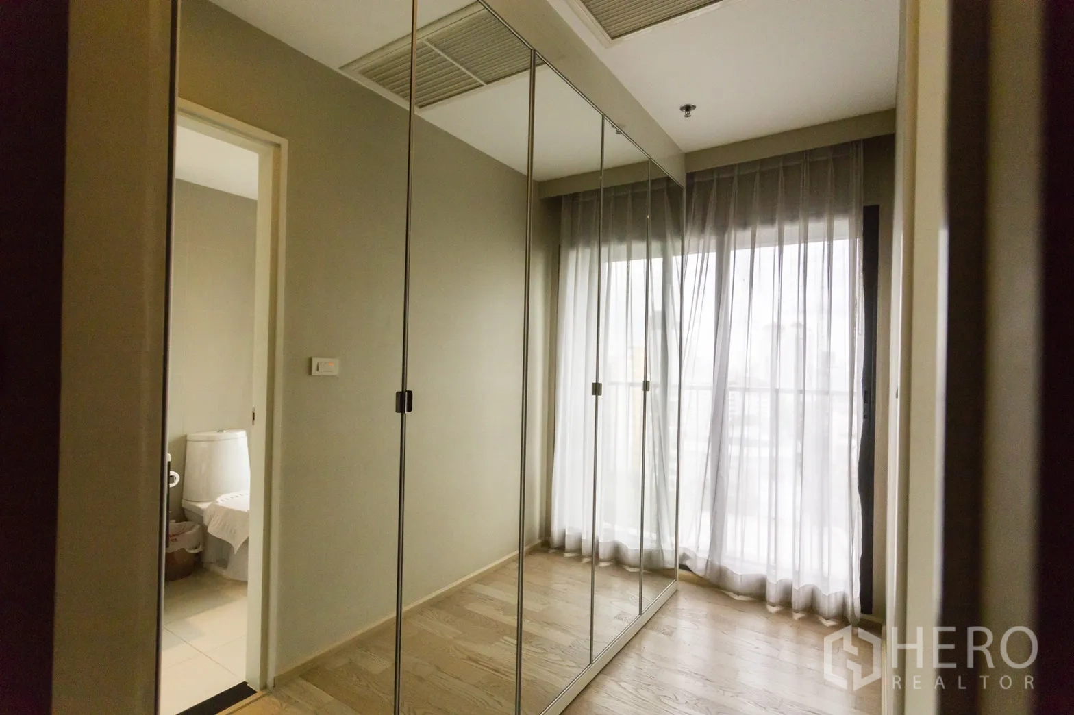 Condominium for rent in Khlong Toei, Bangkok - Hallway with full-height mirrored wardrobes and sheer curtains opening to a balcony.