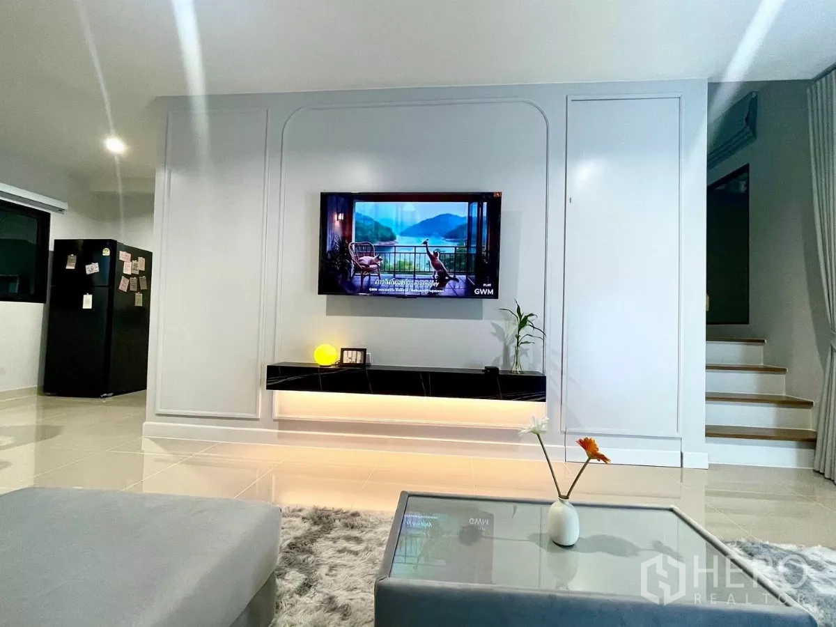 Townhouse for rent in Samut Prakan - Bright living room with TV feature wall, floating cabinet and nearby staircase.