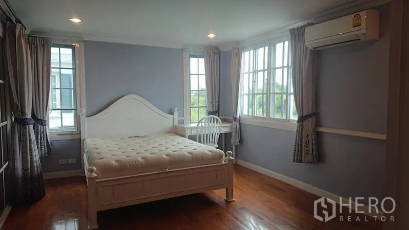 Detached House for rent in Mueang Samut Prakan, Samut Prakan - Airy master bedroom with white bed frame, wood floor, multiple windows and wall air conditioner.
