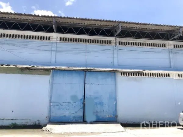 Warehouse for rent in Bang Phli, Samut Prakan - Blue warehouse exterior with large sliding steel gate and ventilation blocks beneath the eaves.