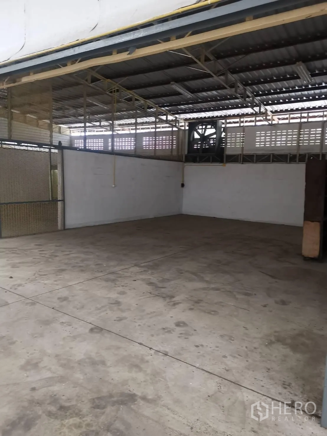 Warehouse for rent in Suan Luang, Bangkok - Semi-open loading bay with concrete floor, mesh partitions and an industrial exhaust fan.