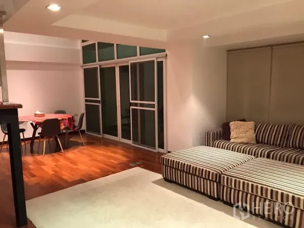 Condominium for rent in Watthana, Bangkok - Open-plan living and dining area with large sliding glass doors and warm hardwood floors.