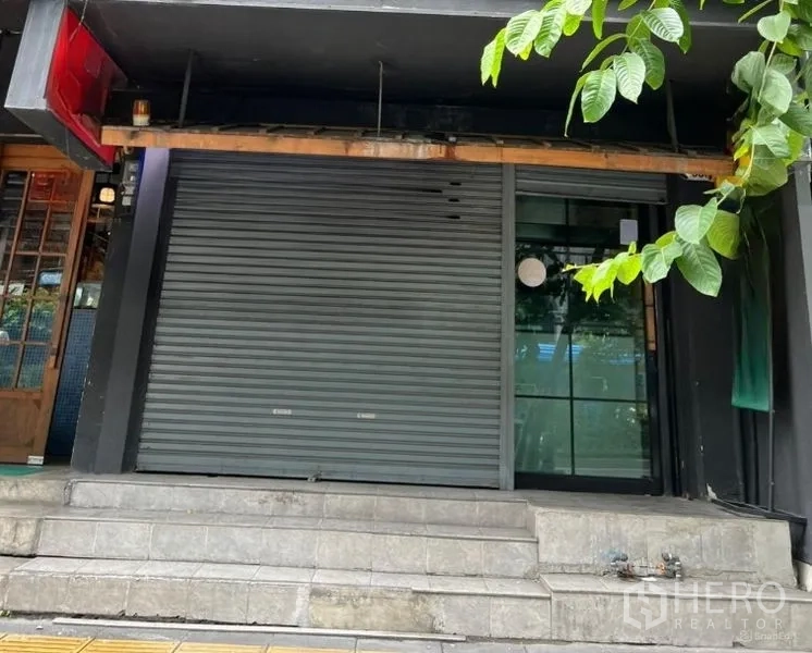 Shophouse for rent in Khlong Toei, Bangkok - Street-level shophouse frontage with roller shutter, glass side door and steps in the Sukhumvit area.