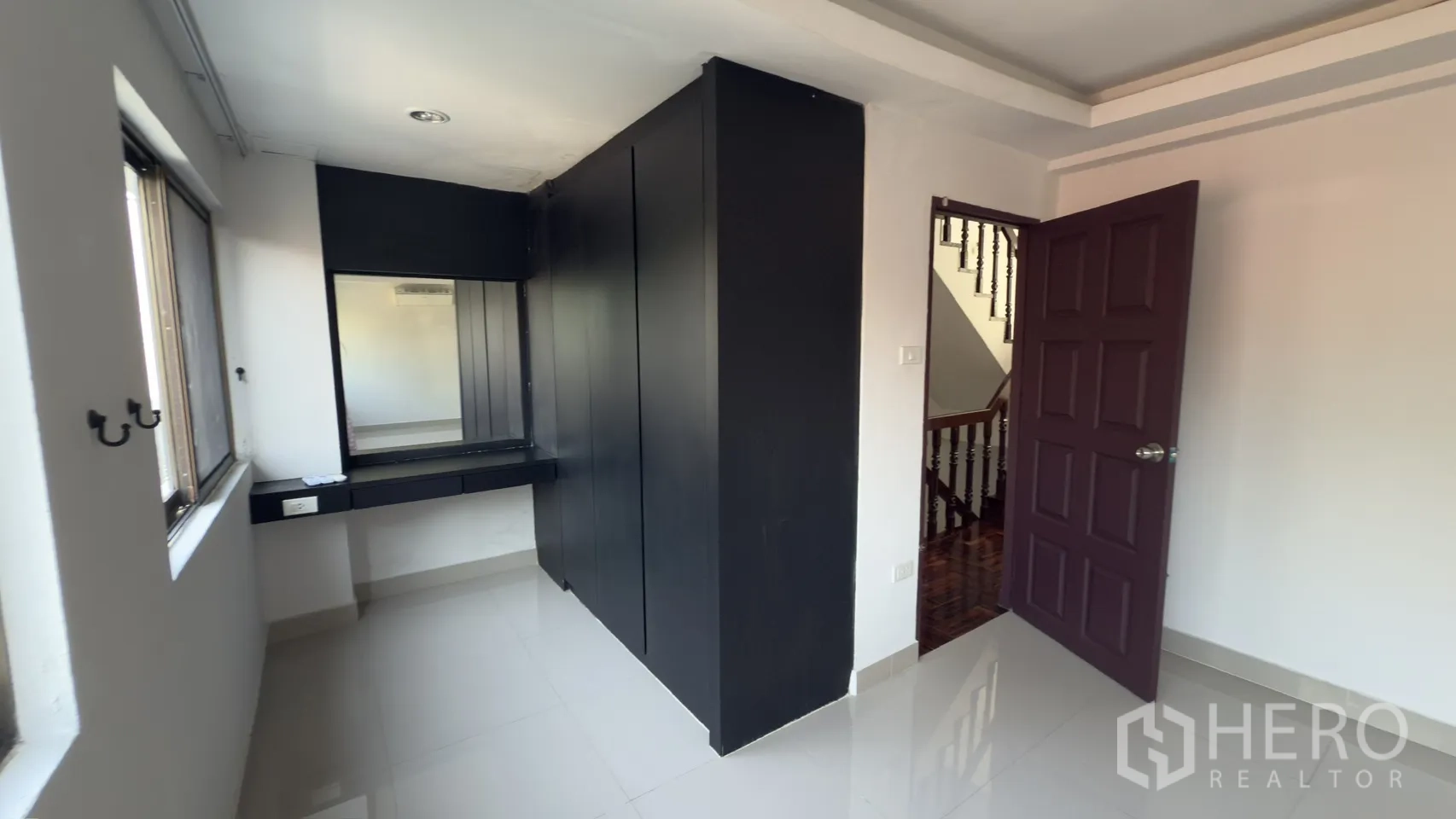 联排别墅 for rent in Watthana, Bangkok - 采光良好的房间，亮面地砖，黑色衣柜与梳妆台，旁边为楼梯。