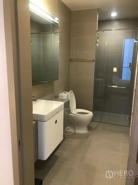 公寓 出租在Pathum Wan, Bangkok - 现代浴室，设洗手台、镜柜、坐便器与玻璃淋浴间，灰色中性瓷砖。