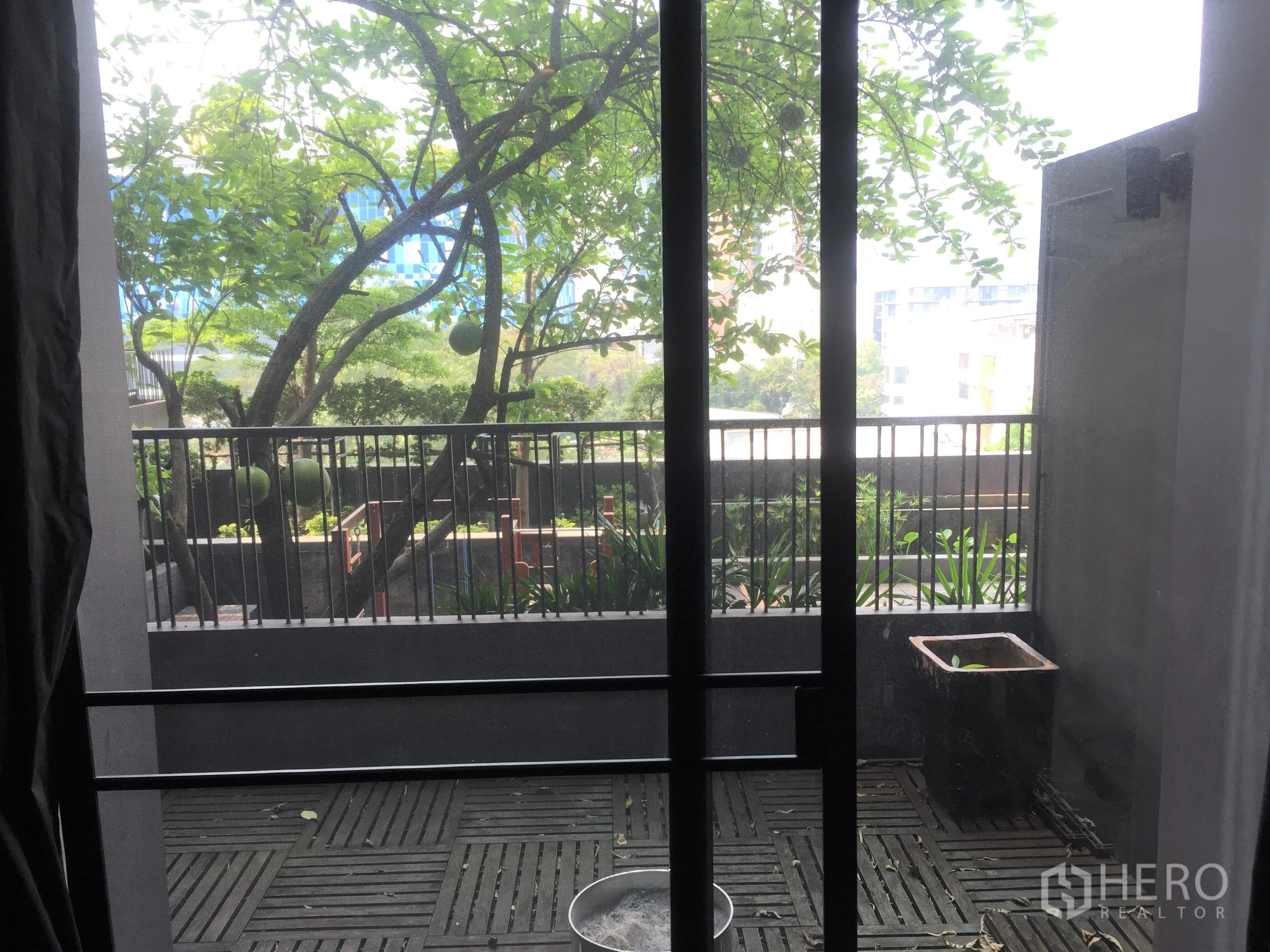 公寓 出租或出售在Watthana, Bangkok - 带木质地板的私家阳台，俯瞰绿意庭院与部分城市景观。