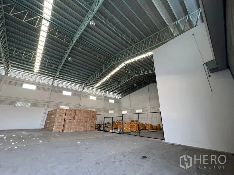 Warehouse for rent in Lat Krabang, Bangkok - Warehouse interior with stacked cartons and a mesh-partitioned storage area under the high ceiling.