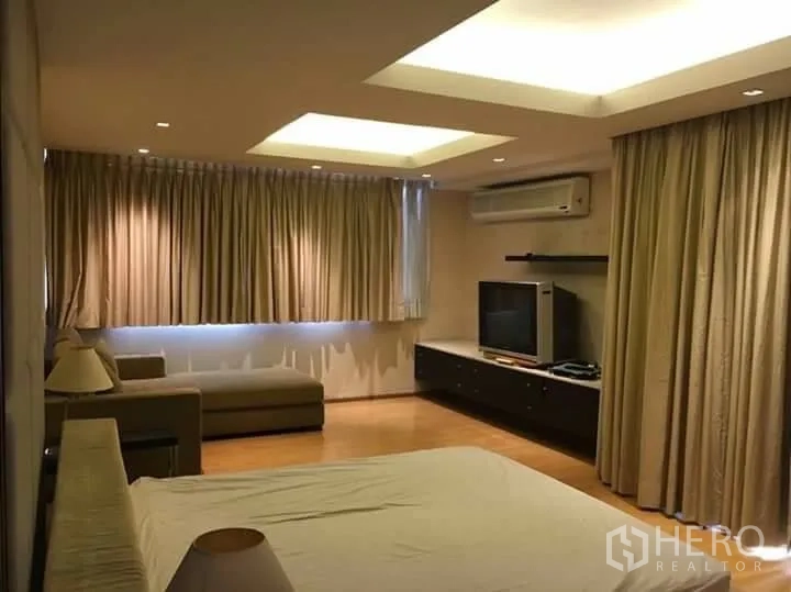 公寓 出租在Watthana, Bangkok - 主卧空间大，带电视柜与沙发，落地窗帘、木地板与嵌灯吊顶。