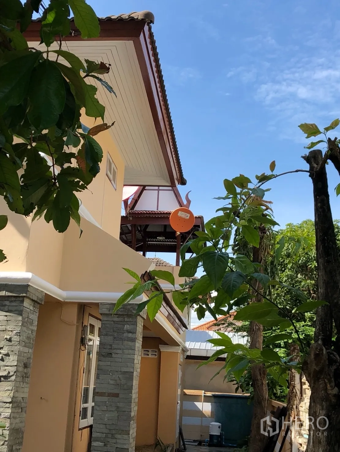 独立式住宅 出租在Min Buri, Bangkok - 侧立面展示石材立柱、挑檐阳台与成树绿荫。