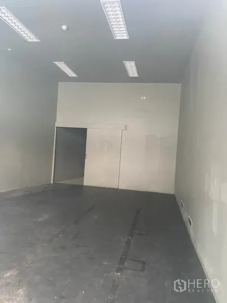 Retail Space for rent in Khlong Toei, Bangkok - Empty retail unit with high ceiling, fluorescent lighting, and concrete floor.