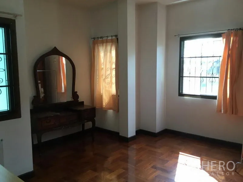 独立式住宅 出租或出售在Huai Khwang, Bangkok - 明亮卧室，实木拼花地板，两扇挂帘窗户与复古梳妆台。