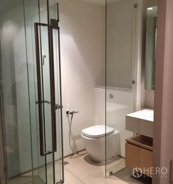 Condominium for rent or sale in Khlong San, Bangkok - Contemporary bathroom with glass shower enclosure, vanity, and toilet.