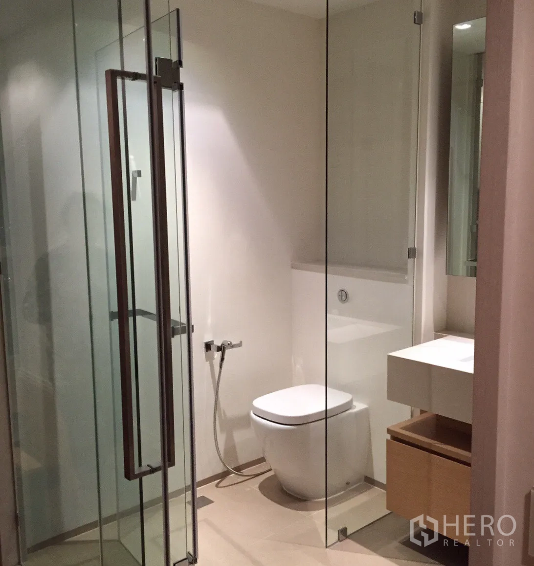 Condominium for rent or sale in Khlong San, Bangkok - Contemporary bathroom with glass shower enclosure, vanity, and toilet.